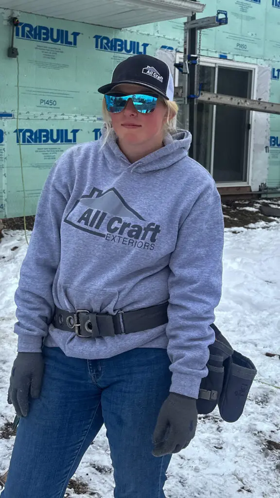 Micayla wearing a tool belt and safety sunglasses on a jobsite during Women in Construction Week at All Craft Exteriors